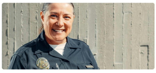 A woman in uniform and wearing a badge smiles at the camera